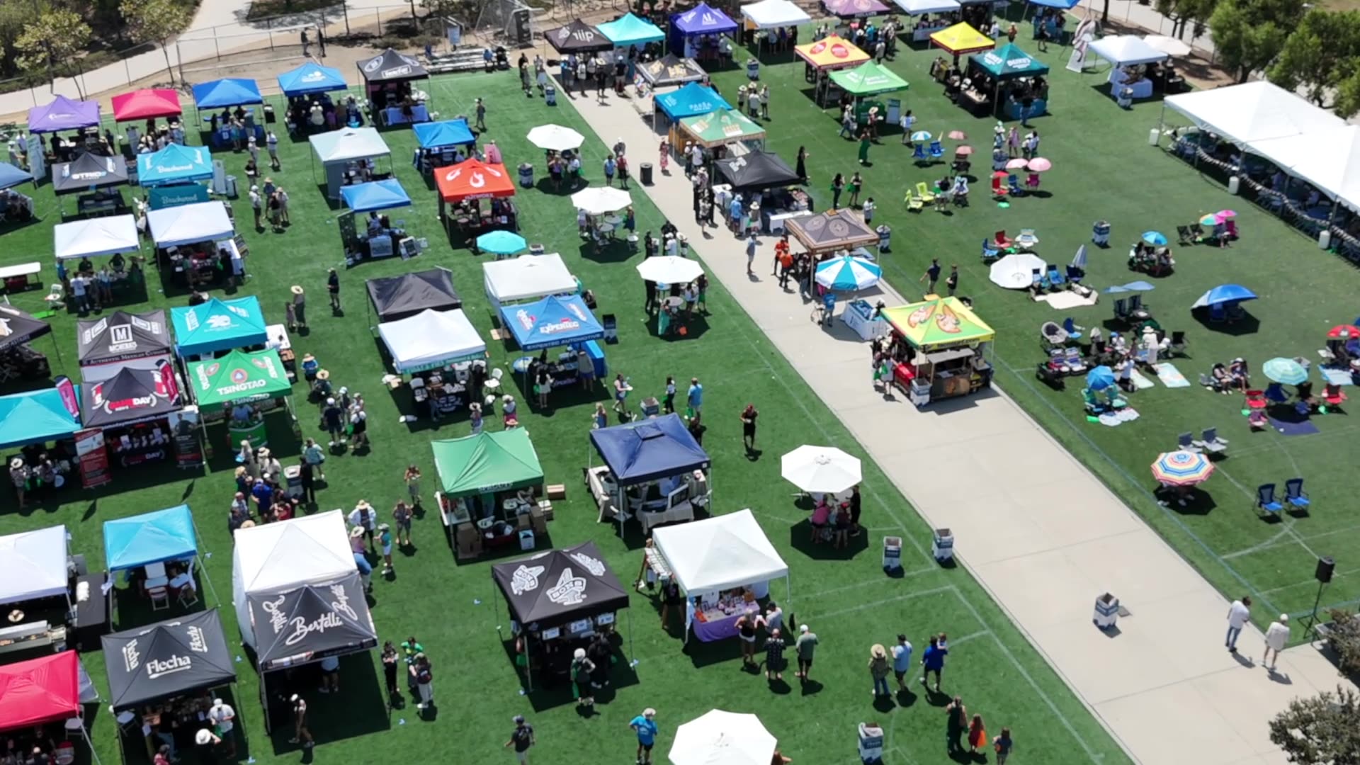 An aerial of easy-up tents with colorful canopies arrayed in a park.