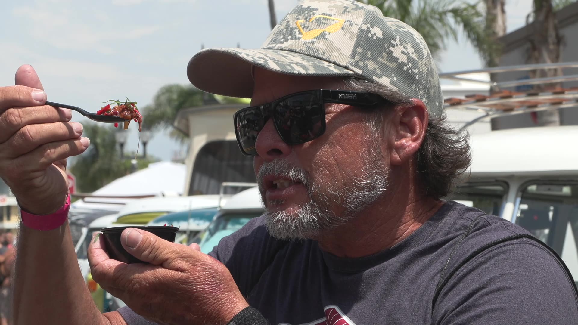 A man in a ballcap holds up a spoonful of chili to inspect